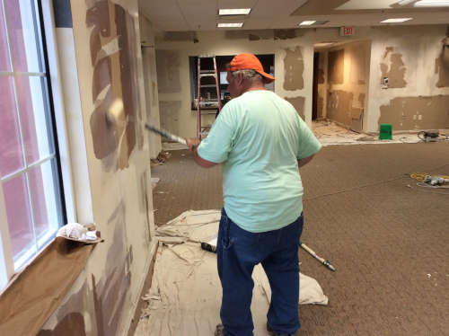 Photo of Scott rolling a sealant over the rough part of a wall in the office.