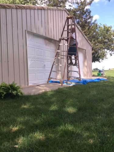 Photo of Scott carefully painting a section of siding that outcrops a steep roof.