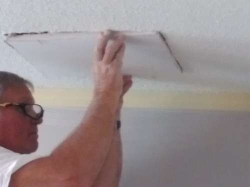A close-up shot of Scott fitting the drywall patch snuggly into place.